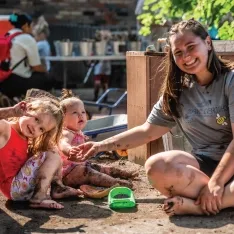 A women sitting with two young children, smiling and playing together outdoors.